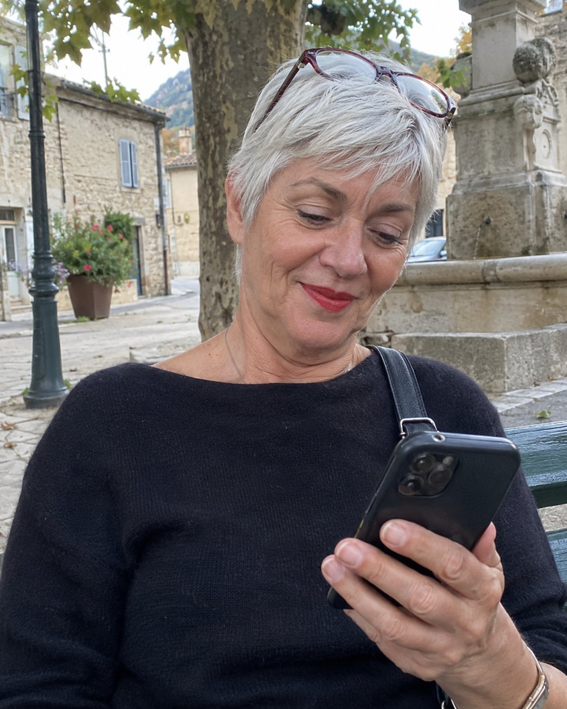 Femme de 62 ans aux cheveux argentés qui regarde son téléphone sur un banc (photo d'illustration)