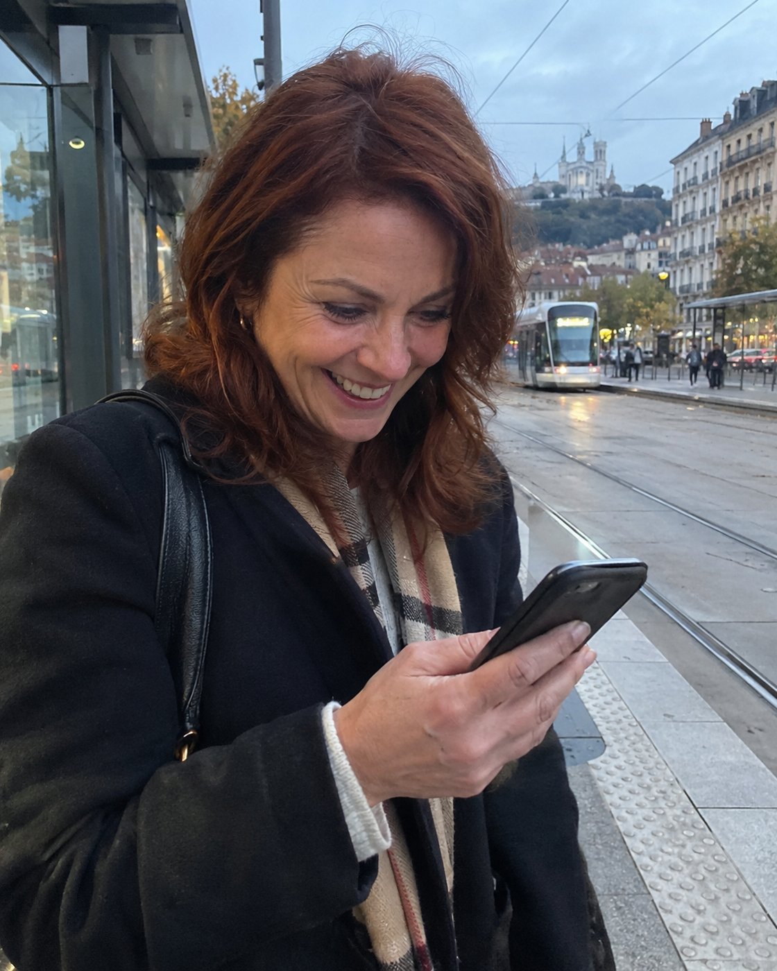 Femme de 51 ans qui sourit à un message en attendant le tram (photo d'illustration)